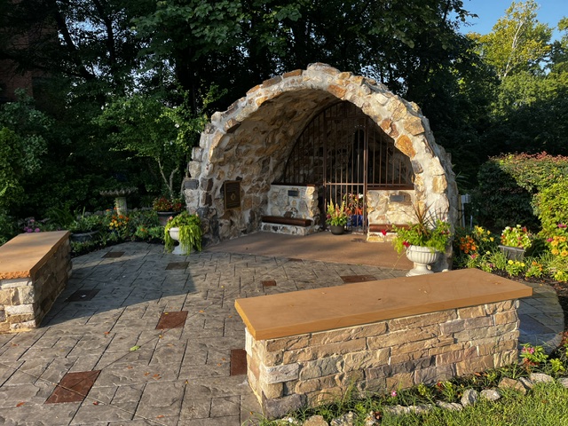 The stone grotto at St. Ann in evening light, with paved courtyard, stone benches, and flower beds