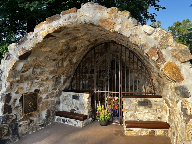 The grotto's fieldstone arch and iron gate, flanked by memorial plaques and stone benches